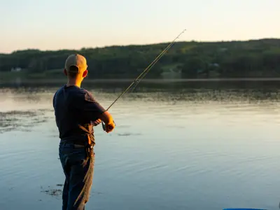 A young adult holding a fishing rod with a line into the water at sunset as seen from Montney Centennial Park