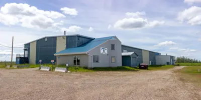 Exterior view of the Clearview Arena in Goodlow, British Columbia. The building features grey horizontal siding, a bright blue metal roof, and several large windows under a partly cloudy sky.