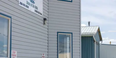 Exterior view of the Clearview Arena in Goodlow, British Columbia. The building features grey horizontal siding, a bright blue metal roof, and several large windows under a partly cloudy sky.